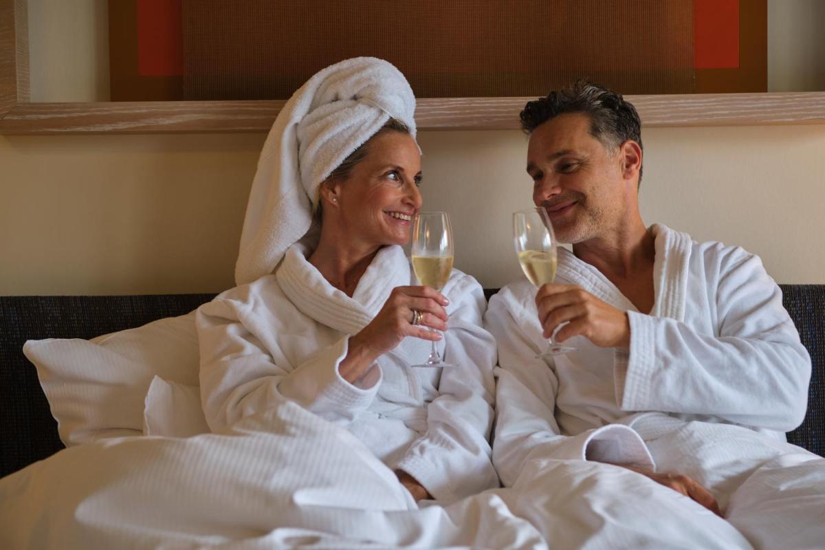 Ein Mann und eine Frau sitzen im Bett und trinken Wein. in der Unterkunft Aalernhüs hotel & spa in Sankt Peter-Ording