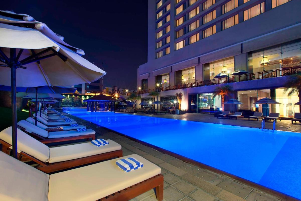 a swimming pool with chairs and umbrellas next to a building at The Westin Hyderabad Mindspace in Hyderabad