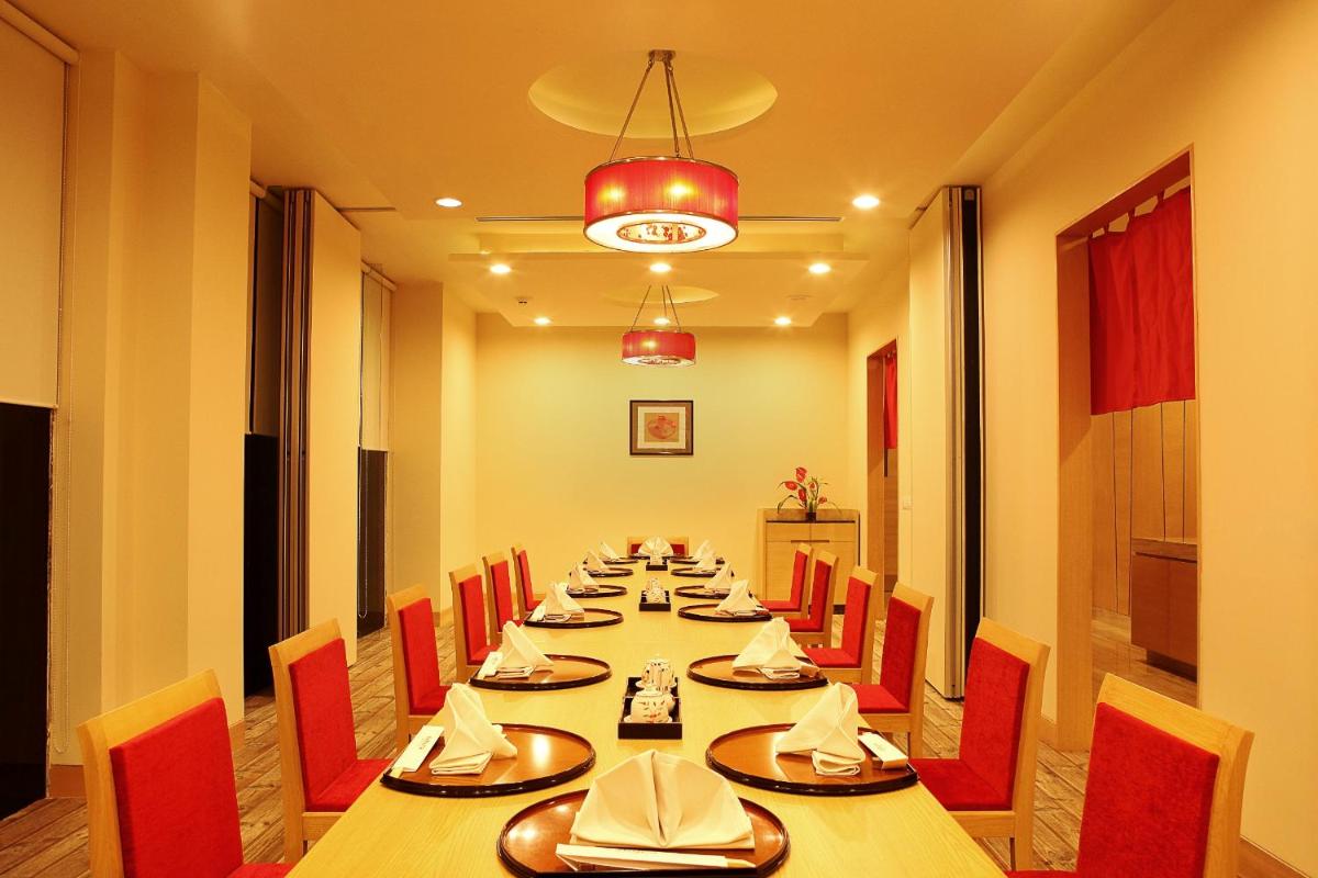 a long dining room with a long table and red chairs at The Metropolitan Hotel & Spa New Delhi in New Delhi