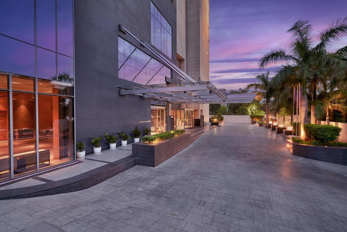 a building with a walkway with palm trees in front at Hyatt Regency Lucknow Gomti Nagar in Lucknow