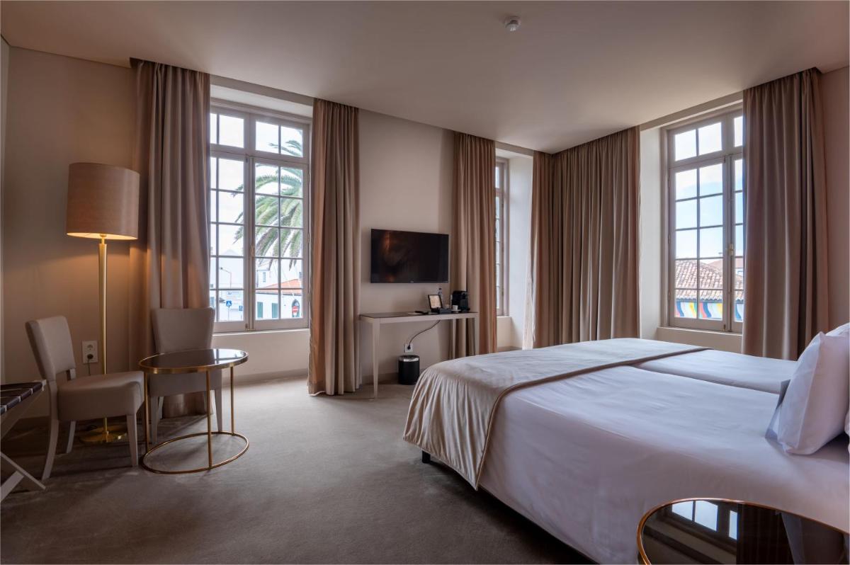 um quarto de hotel com uma cama, uma escrivaninha e janelas em Vila Gale Collection S.Miguel em Ponta Delgada