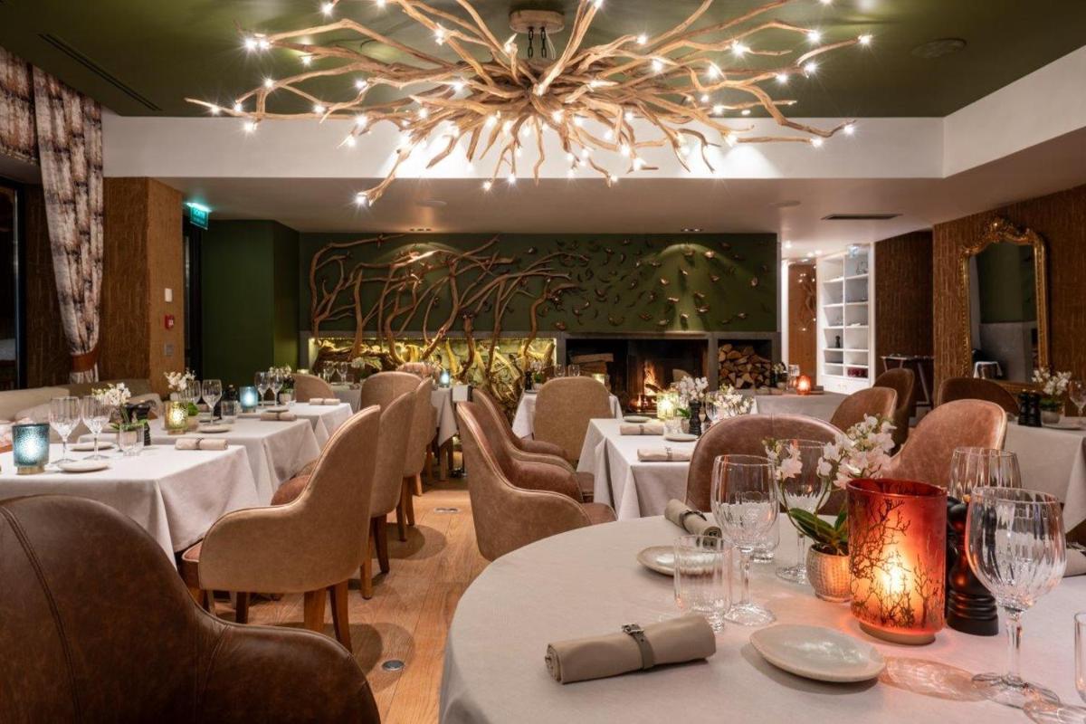 un restaurant avec des tables et des chaises blanches et un lustre dans l'établissement Hôtel La Sivolière, à Courchevel un restaurant avec des tables et des chaises blanches et un lustre dans l'établissement Hôtel La Sivolière, à Courchevel