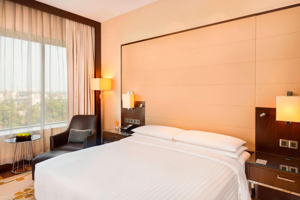 a bedroom with a bed and a chair and a window at Kochi Marriott Hotel in Cochin