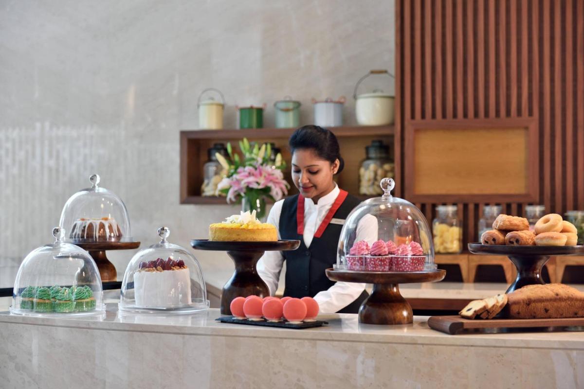 a chef standing behind a counter with cakes and pastries at Kochi Marriott Hotel in Cochin
