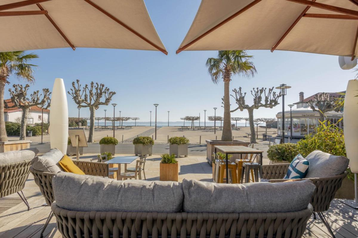 un patio avec des chaises, des tables et des parasols dans l'établissement Hôtel Côté Sable, à Cap-Ferret