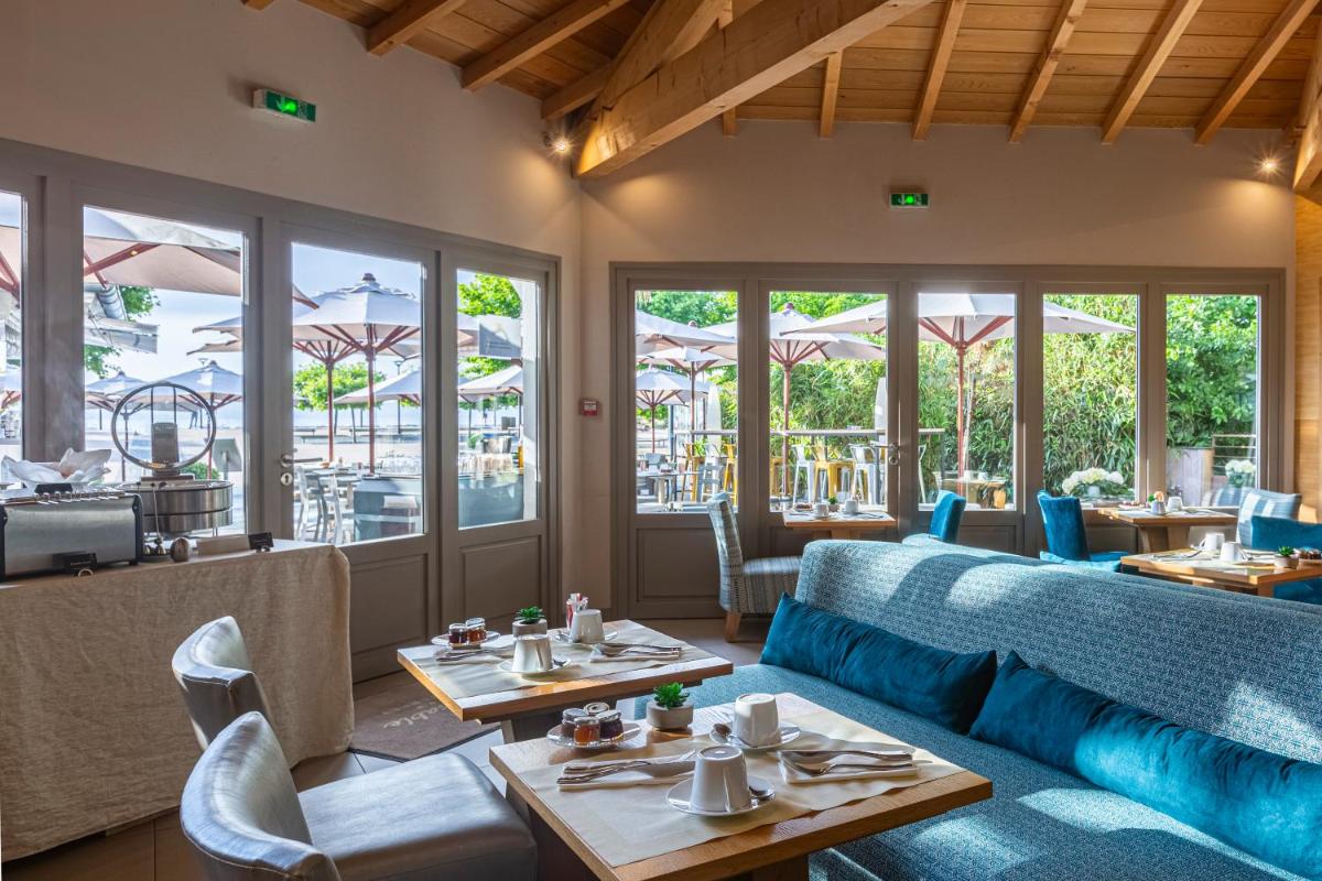 un restaurant avec des canapés bleus, des tables et des fenêtres dans l'établissement Hôtel Côté Sable, à Cap-Ferret