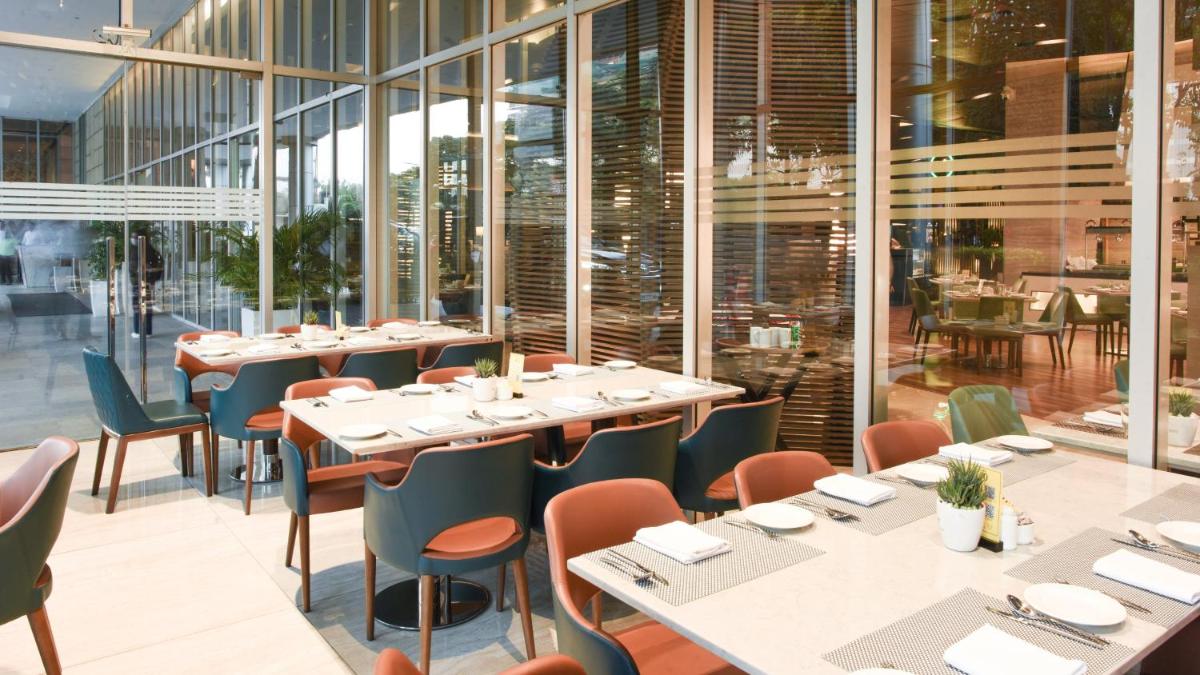 a restaurant with tables and chairs and windows at Holiday Inn New Delhi Aerocity by IHG in New Delhi