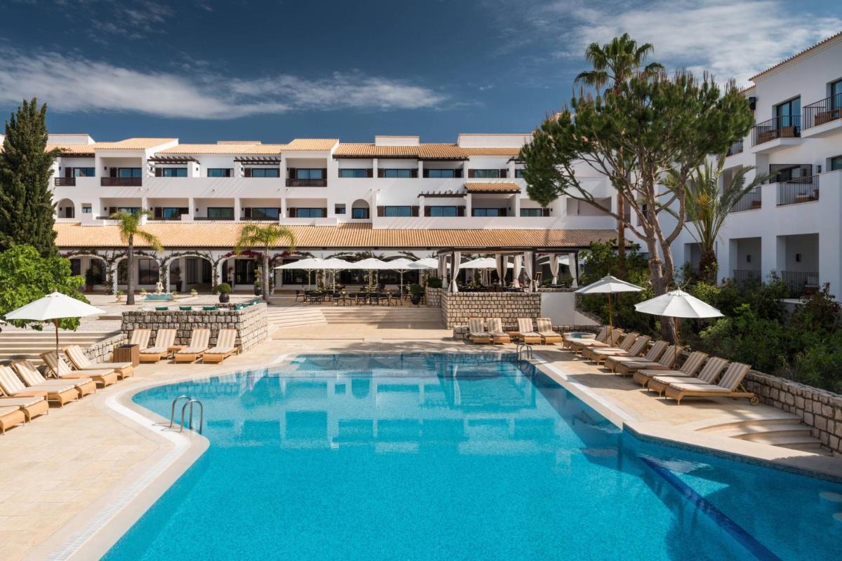 uma piscina em um hotel com cadeiras e guarda-sóis em Pine Cliffs Hotel, a Luxury Collection Resort, Algarve em Albufeira uma piscina em um hotel com cadeiras e guarda-sóis em Pine Cliffs Hotel, a Luxury Collection Resort, Algarve em Albufeira