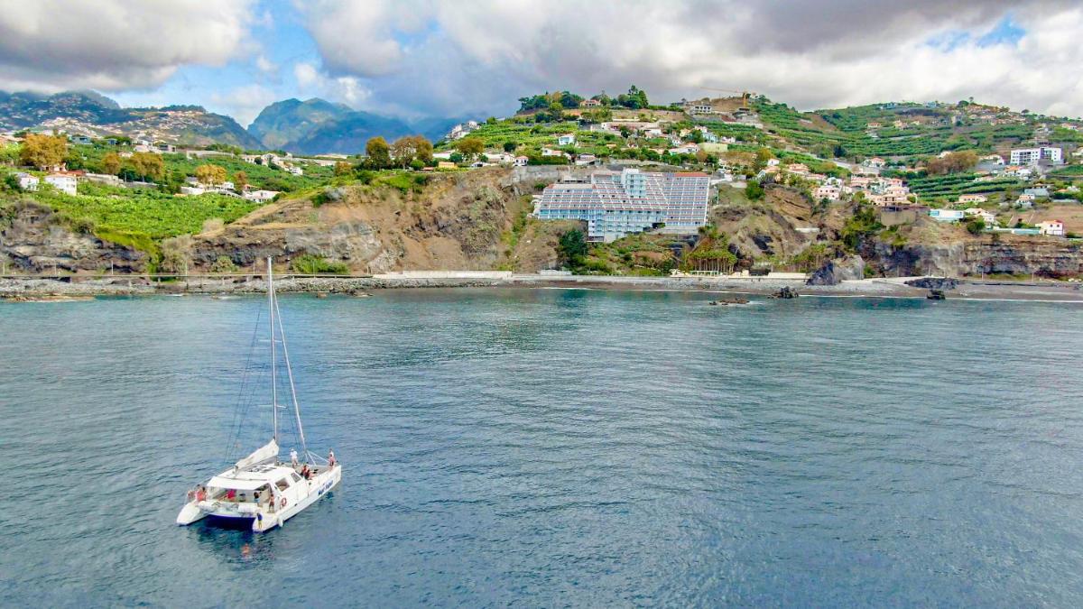 um barco flutuando em um corpo de água com uma montanha em Hotel Orca Praia no Funchal