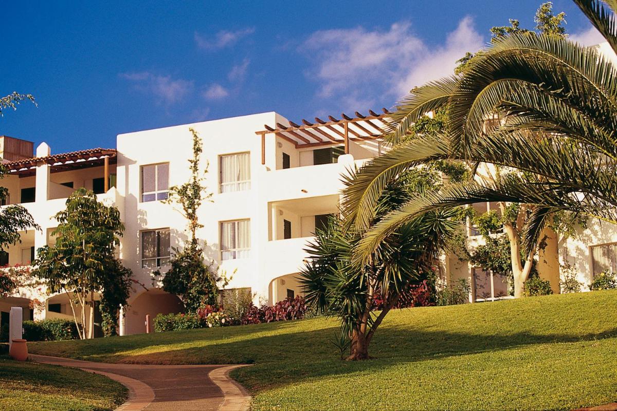 Un gran edificio blanco con una palmera delante. en ROBINSON ESQUINZO PLAYA - All Inclusive, en Morro del Jable