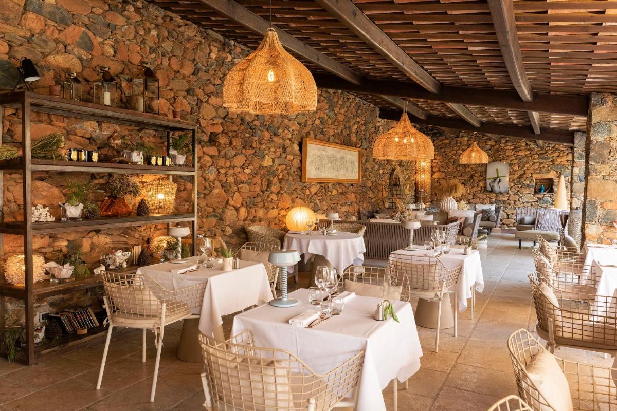 un restaurant avec des tables et des chaises blanches et des murs en pierre dans l'établissement Hôtel La Dimora & Spa, à Saint-Florent