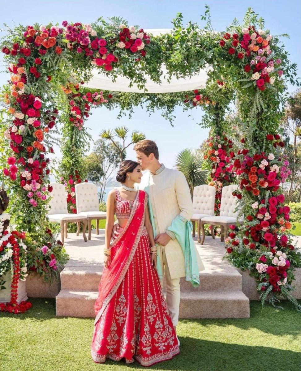 a bride and groom standing under an arch of roses at The Raj Palace (Small Luxury Hotels of the World) in Jaipur