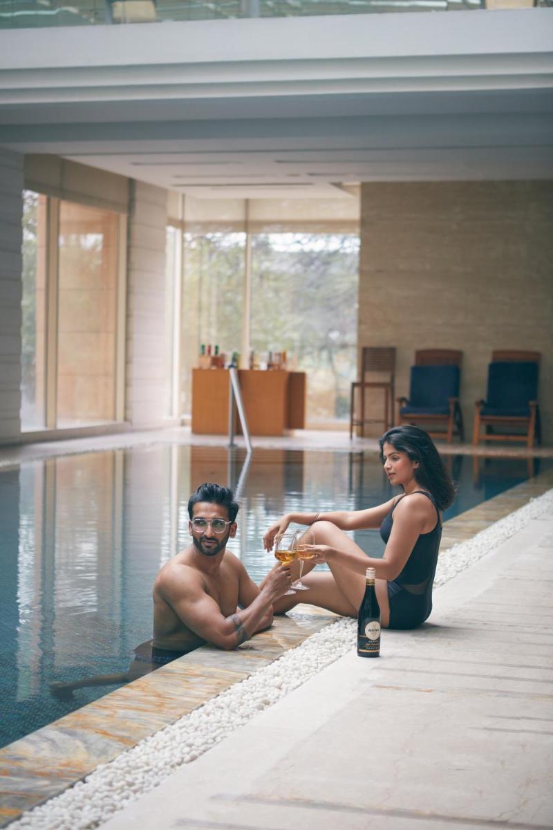 a man and woman sitting in a swimming pool with a bottle of wine at Hyatt Regency Pune Hotel & Residences in Pune