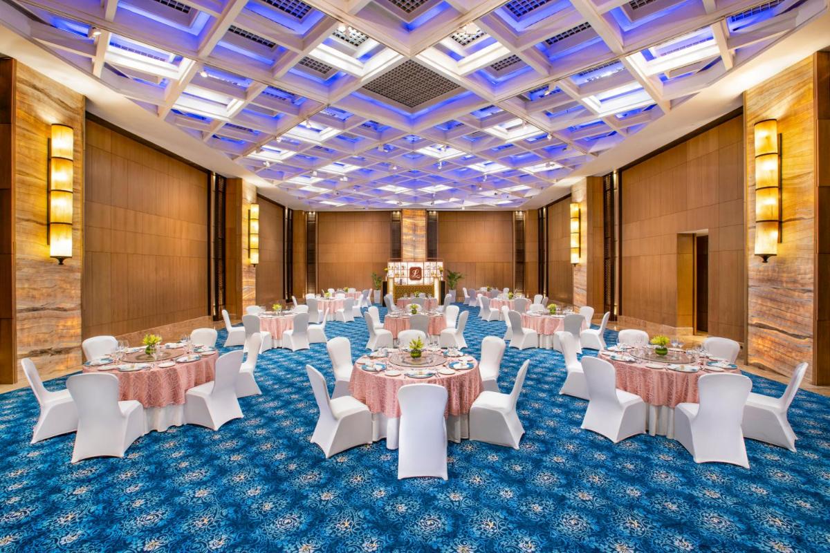 a banquet hall with white tables and white chairs at The Leela Ambience Convention Hotel Delhi in New Delhi