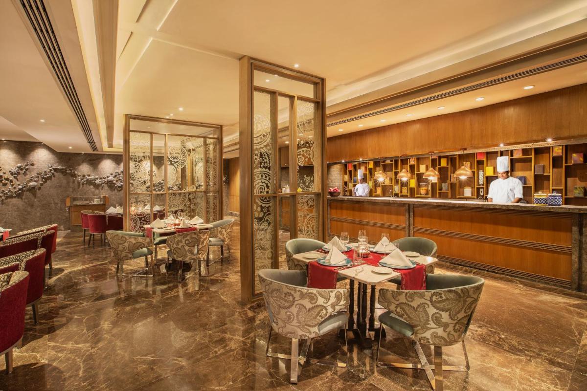 a restaurant with tables and a chef in the background at The Leela Ambience Convention Hotel Delhi in New Delhi