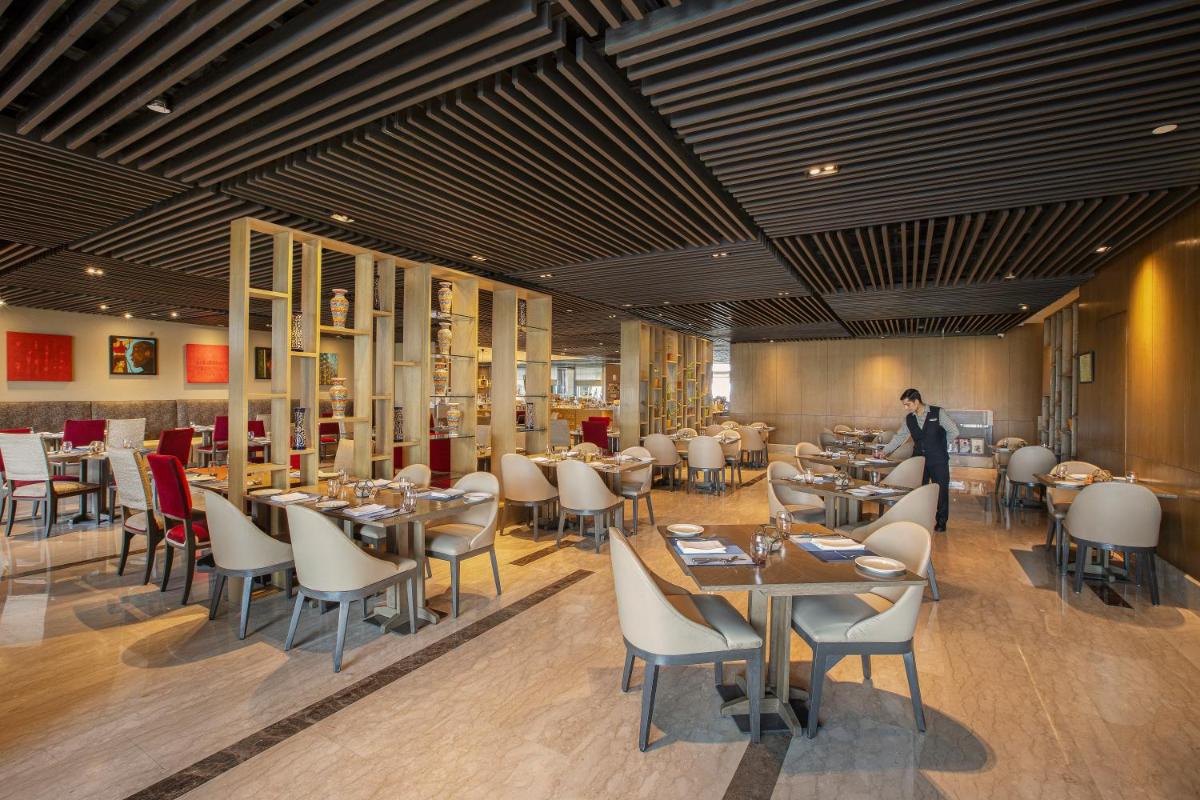 a restaurant with tables and chairs and a person in the background at The Leela Ambience Convention Hotel Delhi in New Delhi