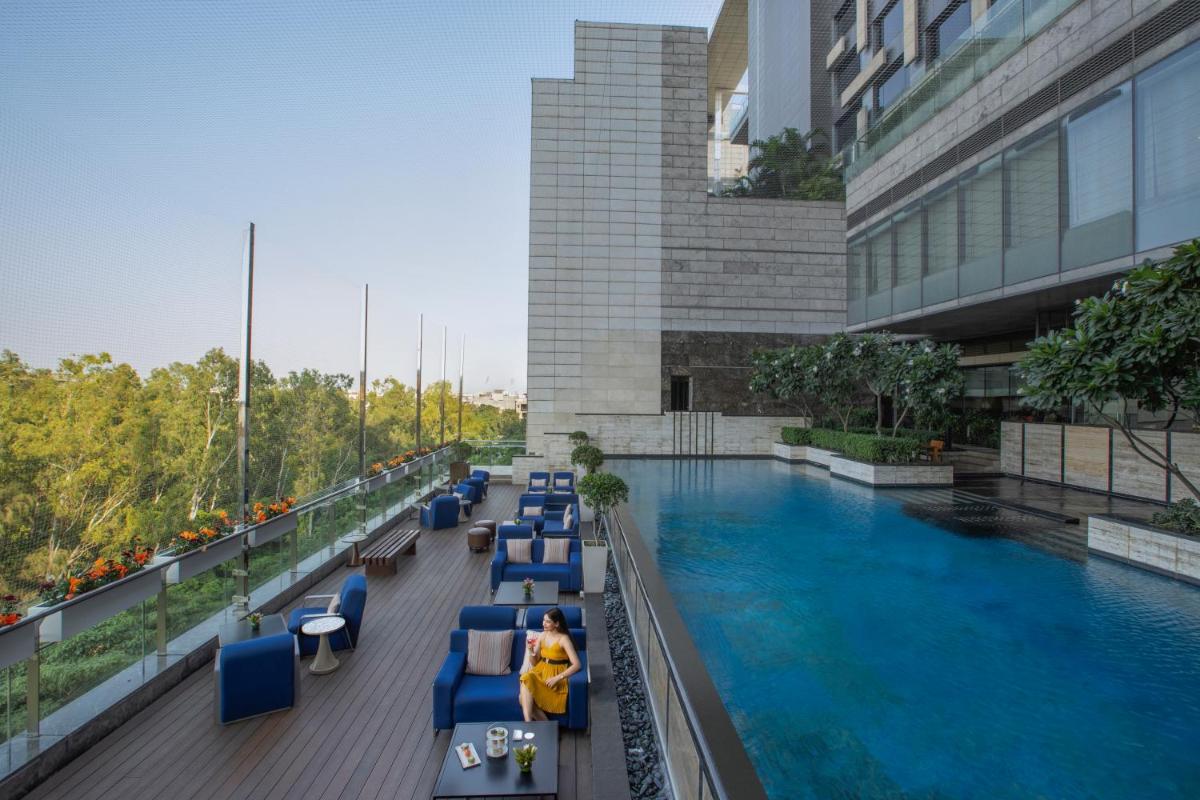 a swimming pool in a building with blue chairs at The Leela Ambience Convention Hotel Delhi in New Delhi
