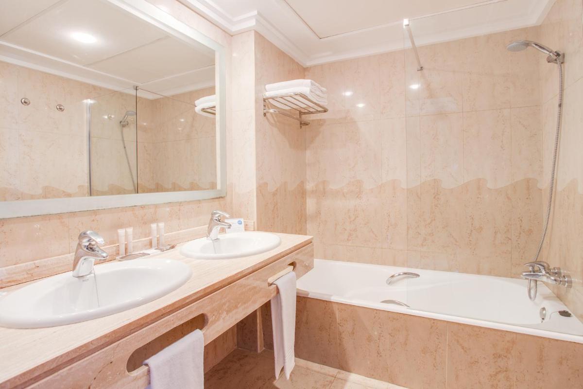 Un baño con dos lavabos, una bañera y un espejo. en Inturotel Sa Marina, en Cala d´Or