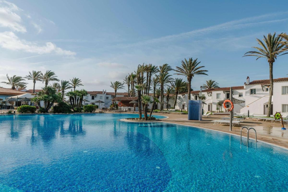 Una gran piscina con palmeras y edificios. en AluaSun Mediterráneo, en S'Algar