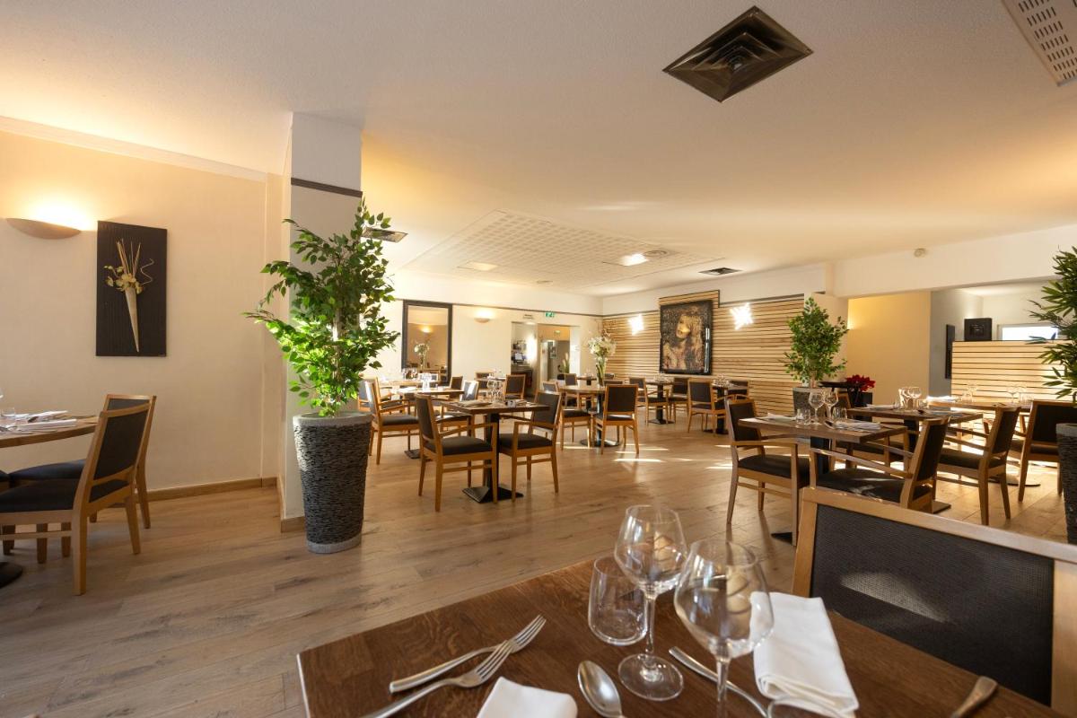 une salle à manger avec des tables et des chaises dans un restaurant dans l'établissement Logis Hotel Restaurant SPA Les Oliviers, à Loriol-sur-Drôme