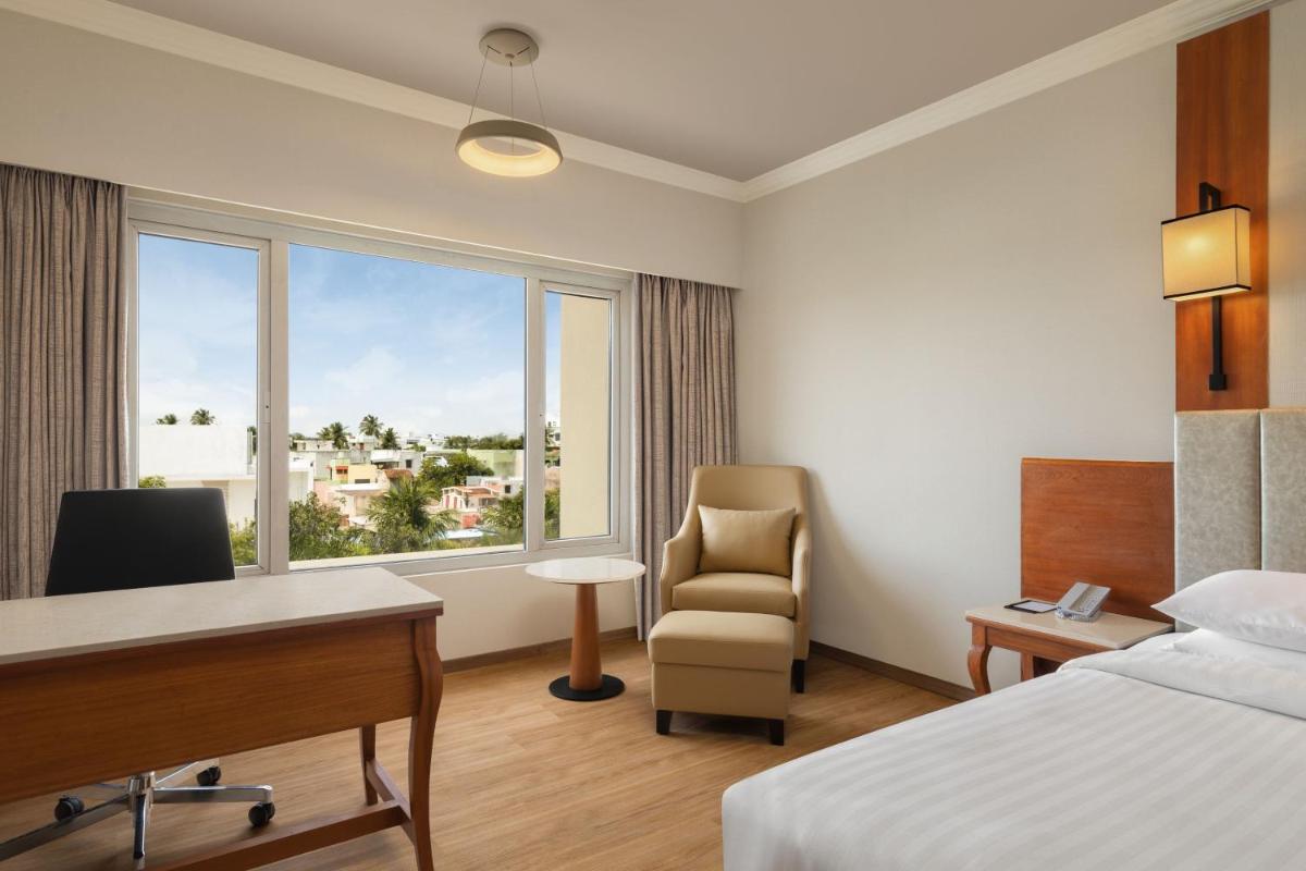 a hotel room with a bed and a desk and a window at Courtyard by Marriott Tiruchirappalli in Tiruchchirāppalli