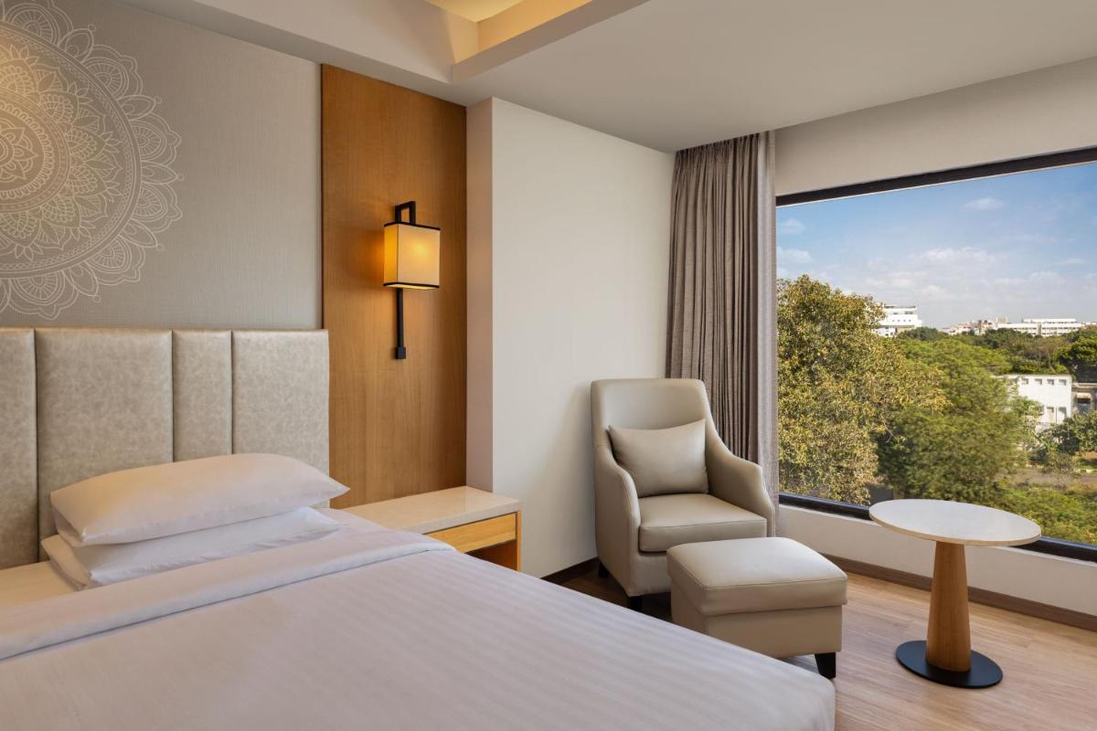 a bedroom with a bed and a chair and a window at Courtyard by Marriott Tiruchirappalli in Tiruchchirāppalli