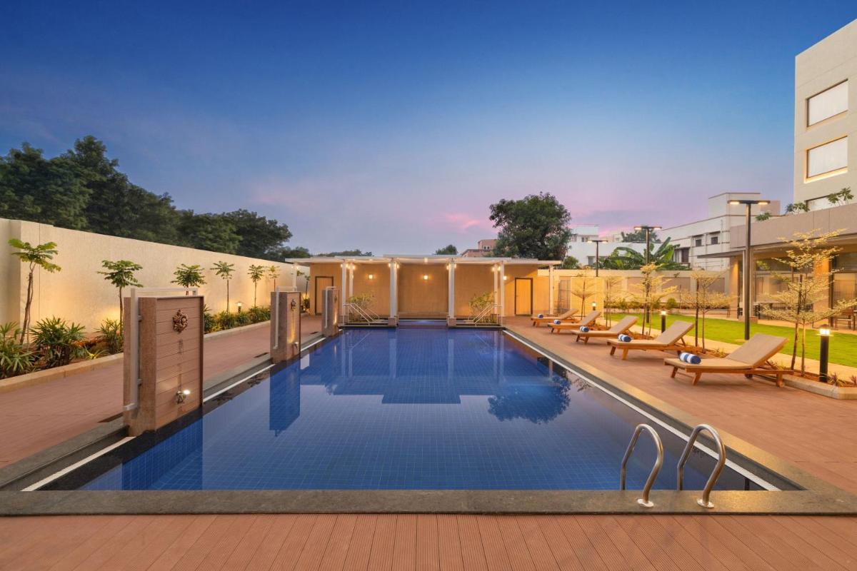 a swimming pool with chairs and a building at Courtyard by Marriott Tiruchirappalli in Tiruchchirāppalli