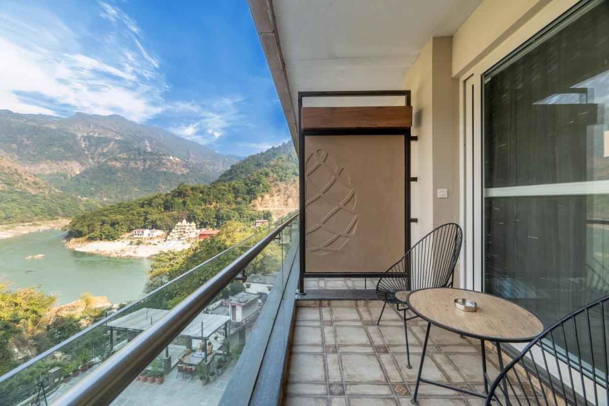 a balcony with a table and chairs and a view of a river at Antalya By Divine Ganga Cottage in Rishīkesh