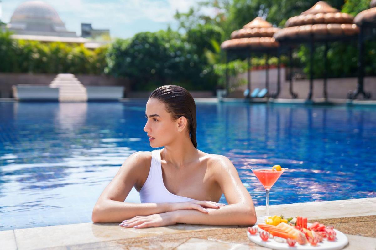 a woman sitting in a pool with a plate of food and a drink at Taj Krishna in Hyderabad