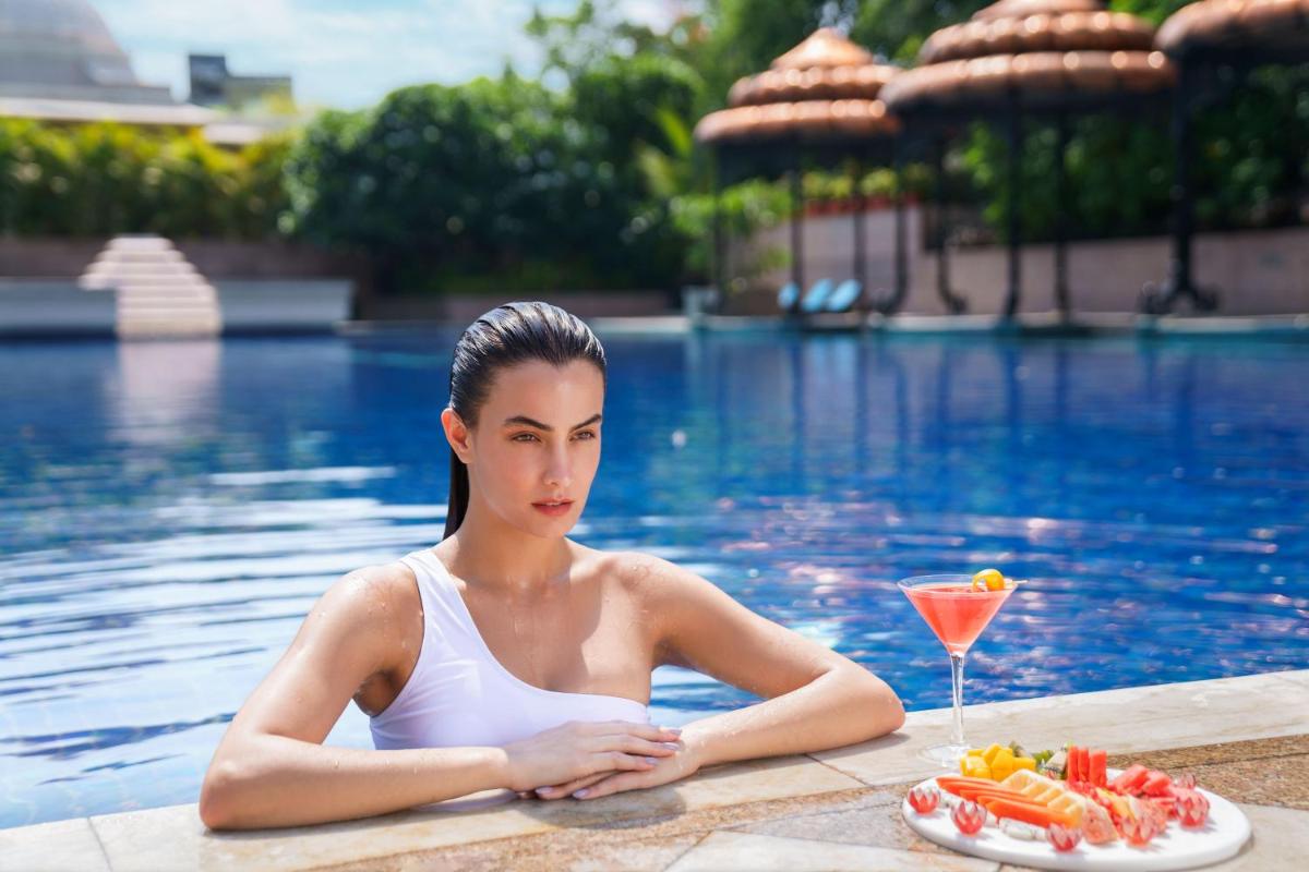 a woman in a swimming pool with a plate of food and a drink at Taj Krishna in Hyderabad