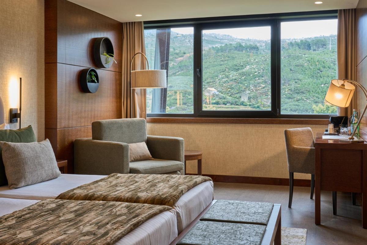 um quarto de hotel com uma cama, uma cadeira e uma janela em H2otel Congress & Medical SPA em Unhais da Serra