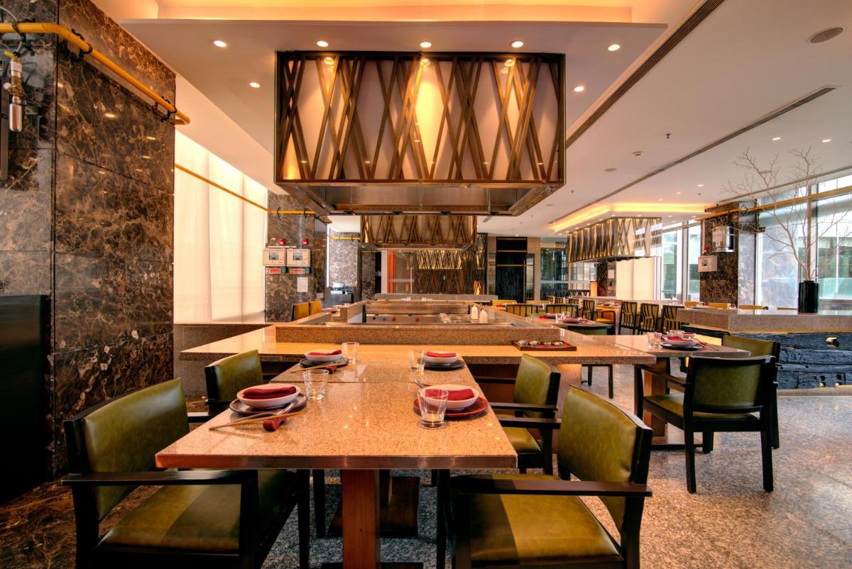 a restaurant with wooden tables and chairs and a chandelier at Hyatt Ahmedabad in Ahmedabad