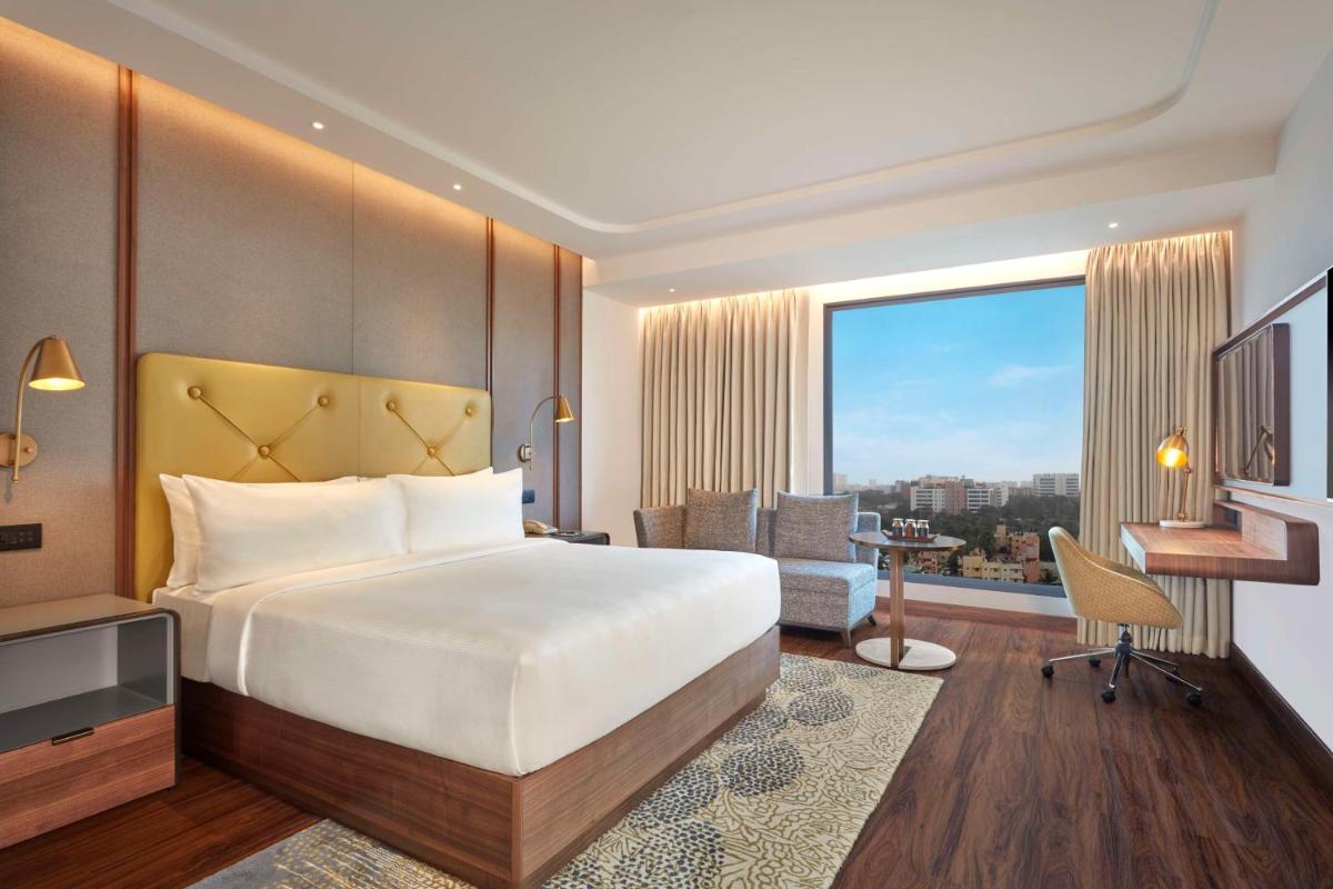 a hotel room with a bed and a desk and a window at Doubletree By Hilton Bengaluru Whitefield in Bengaluru