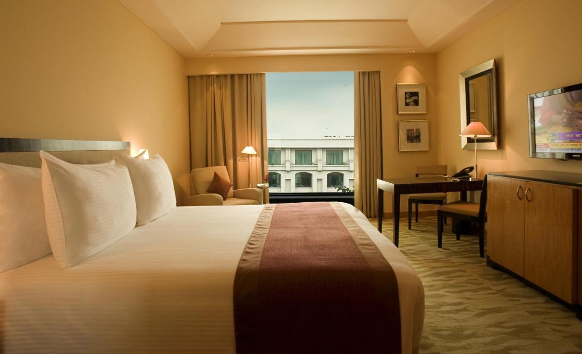 a hotel room with a large bed and a desk at The Grand New Delhi in New Delhi a hotel room with a large bed and a desk at The Grand New Delhi in New Delhi