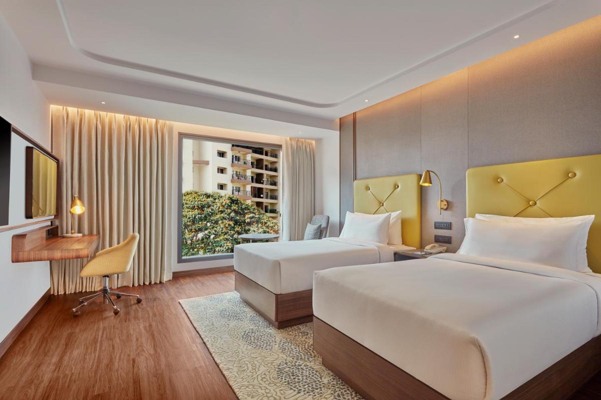a hotel room with two beds and a desk and a window at Doubletree By Hilton Bengaluru Whitefield in Bengaluru