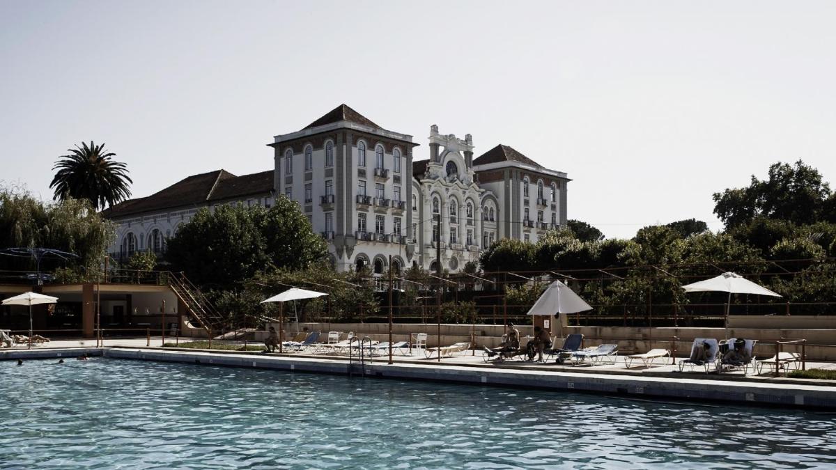 uma piscina com cadeiras e guarda-sóis em frente a um edifício em Curia Palace Hotel & Spa em Curia