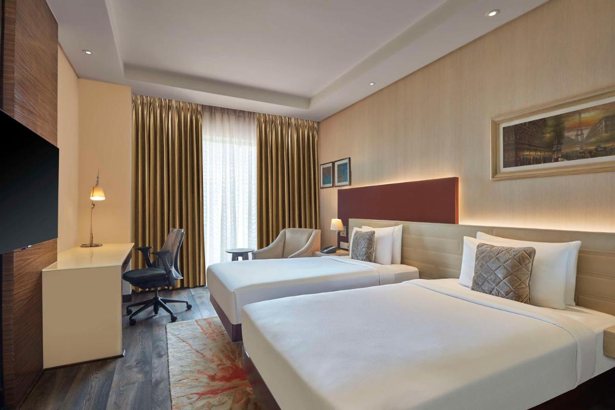 a hotel room with two beds and a desk at DoubleTree by Hilton Gurugram Baani Square in Gurgaon