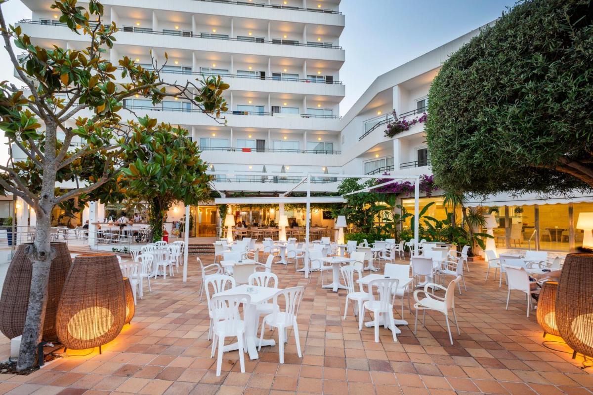 un restaurante con mesas y sillas blancas frente a un edificio en Hotel Morito, en Cala Millor