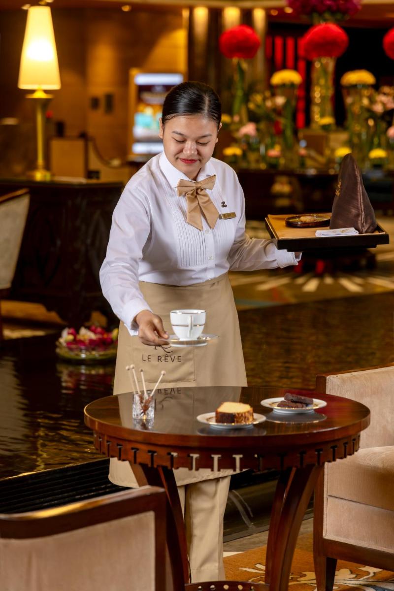 a woman standing next to a table with a plate of food at The Leela Ambience Gurugram Hotel & Residences - The Luxury Urban Sanctuary in Gurgaon