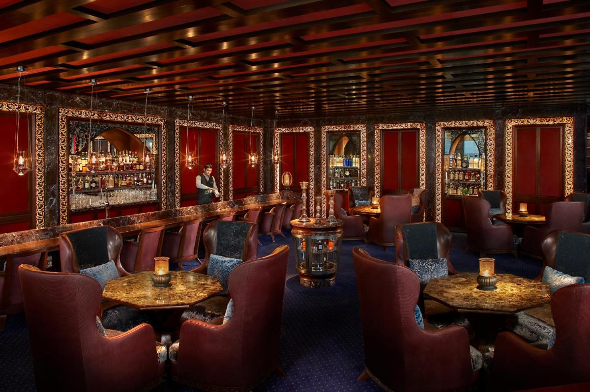 a restaurant with red chairs and tables and a bar at The Leela Ambience Gurugram Hotel & Residences - The Luxury Urban Sanctuary in Gurgaon