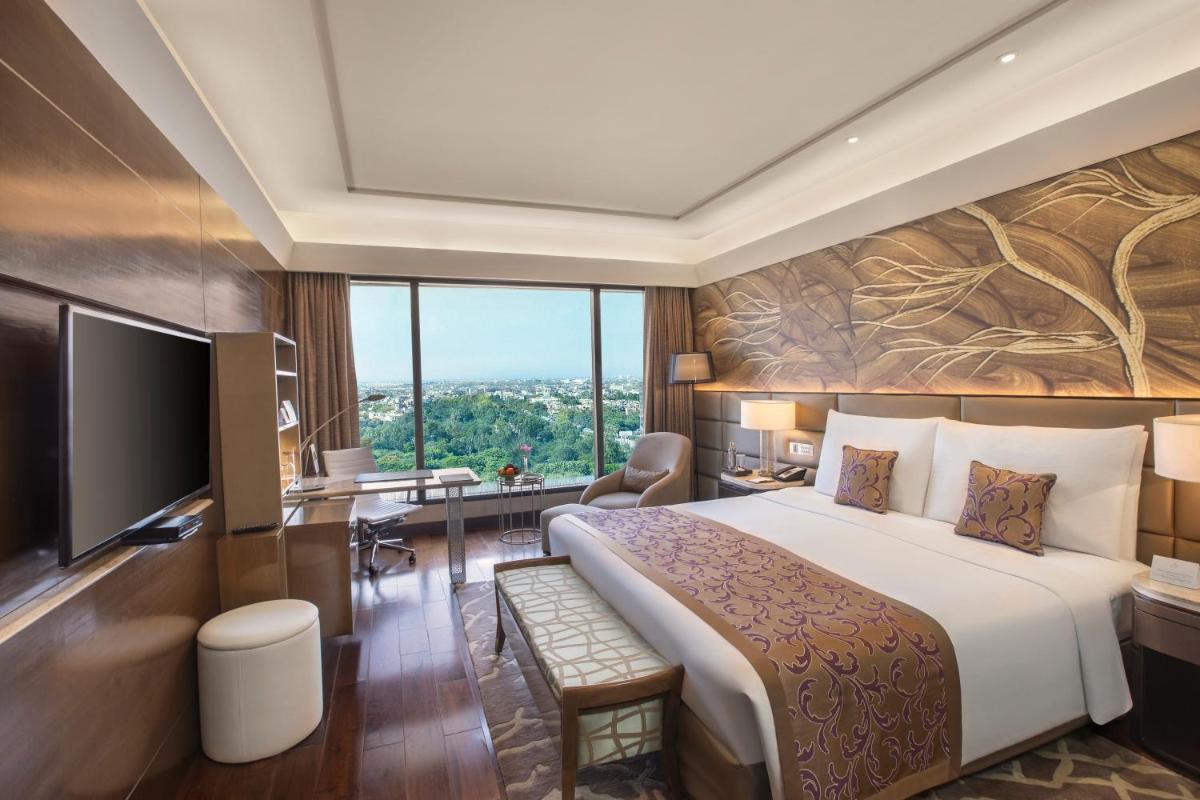 a hotel room with a large bed and a television at The Leela Ambience Convention Hotel Delhi in New Delhi