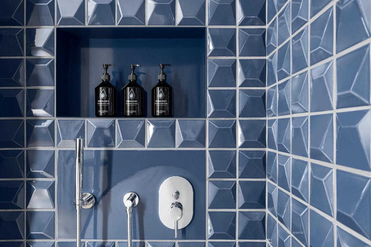 ein blau gefliestes Badezimmer mit drei Flaschen auf einem Regal in der Unterkunft ESPLANADE Saarbrücken in Saarbrücken