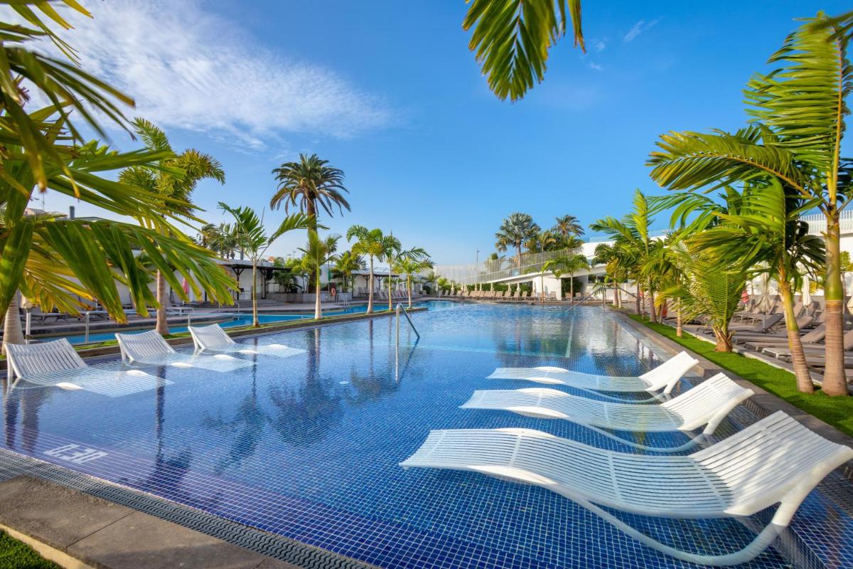 una piscina con sillas blancas y palmeras en Alexandre Troya, en Playa de las Américas