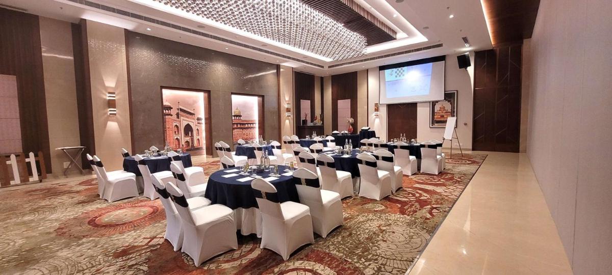 a banquet hall with tables and white chairs and a screen at Radisson Blu Hotel, Greater Noida in Greater Noida