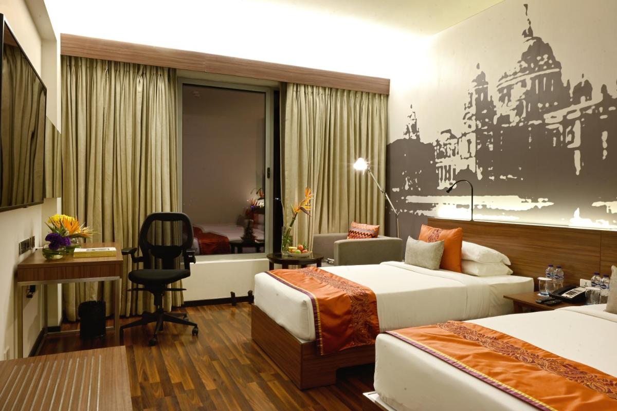 a hotel room with two beds and a desk at Vivanta Kolkata EM Bypass in Kolkata