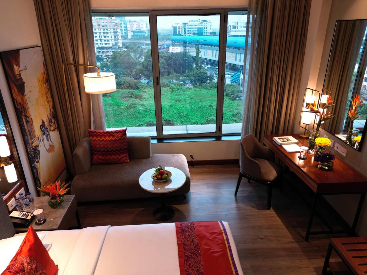 a hotel room with a bed and a desk and a large window at Vivanta Kolkata EM Bypass in Kolkata