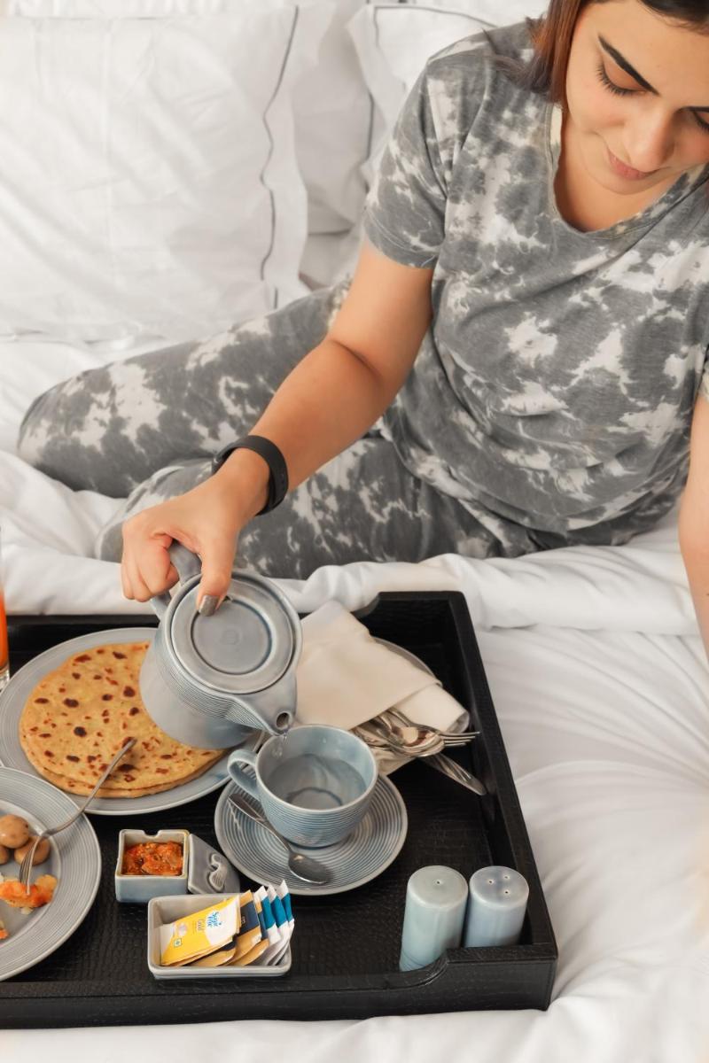 a woman sitting on a bed with a tray of food at The Prominence Mussoorie Road Dehradun in Dehradun