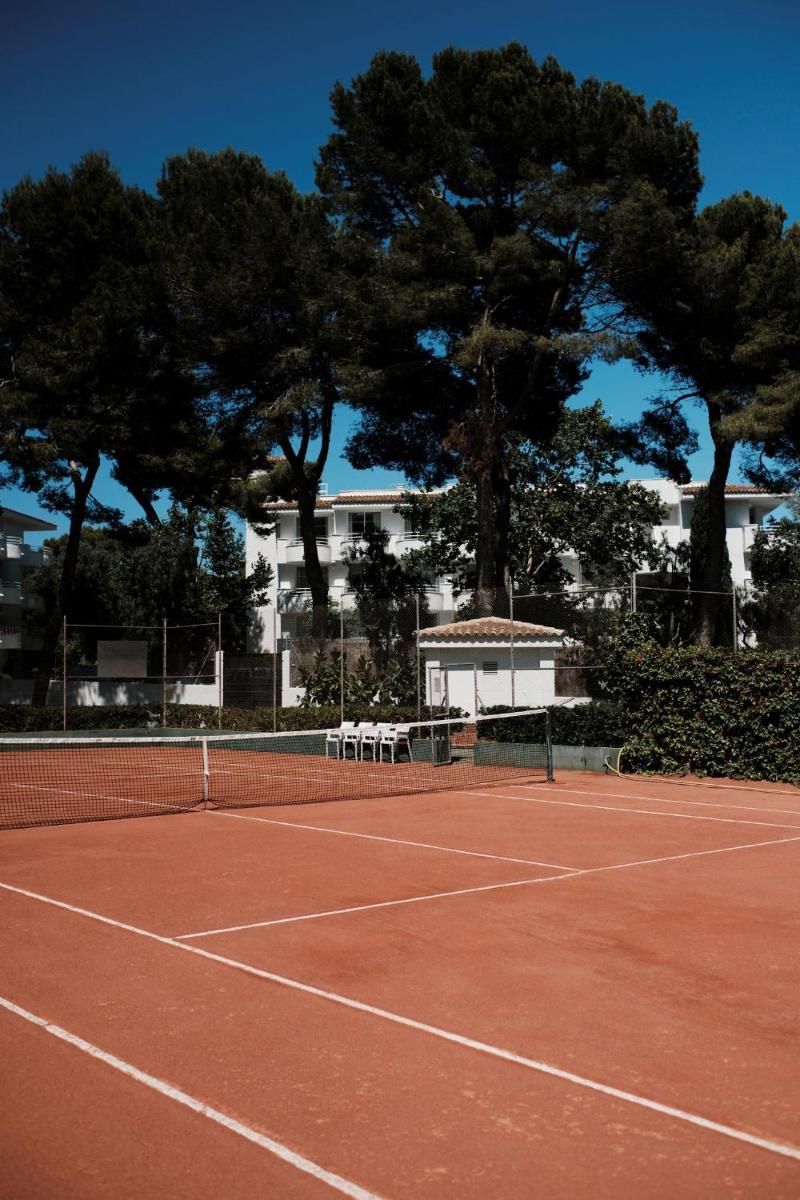 una pista de tenis con árboles en el fondo en Prinsotel La Pineda, en Cala Ratjada