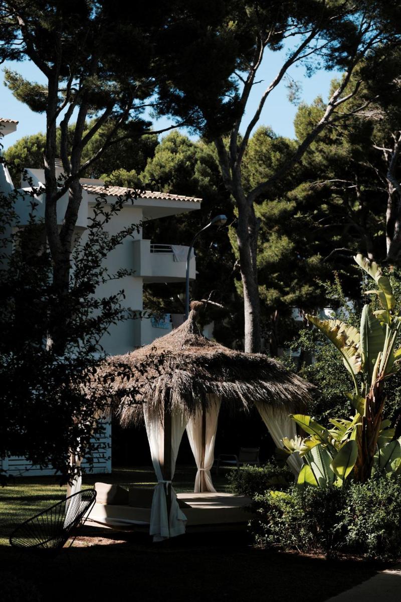 una cabaña de paja en un parque con árboles y un edificio en Prinsotel La Pineda, en Cala Ratjada