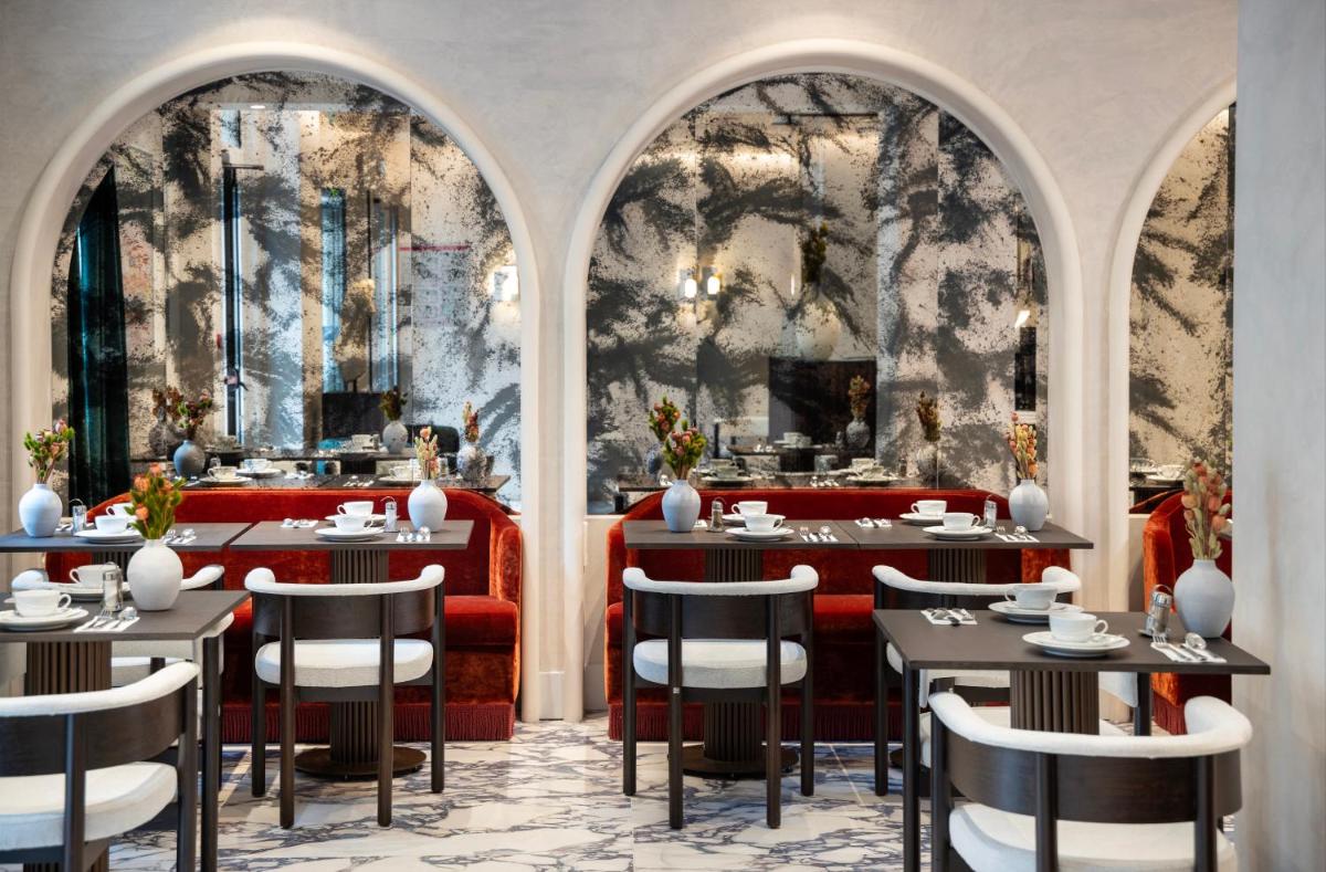 un restaurant avec des fenêtres cintrées, des tables et des chaises dans l'établissement Hotel des Carmes by Malone, à Paris